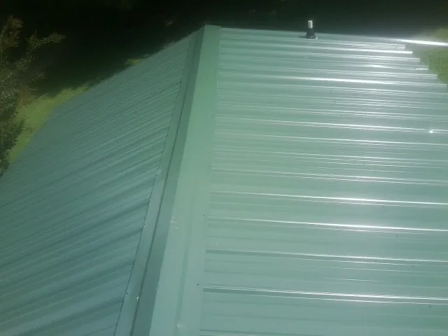 New green metal panels meeting at the ridge of a roof — Flat Roof Repair work by our crew in New Waverly